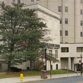 A view of a hospital building with trees and a fire hydrant on the sidewalk.