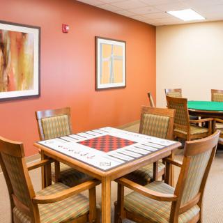 A cozy game room with a table set for board games, surrounded by comfortable chairs and decorated with artwork on the walls.