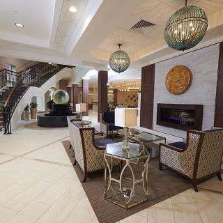 A modern hotel lobby with elegant seating, decorative lighting, and a grand staircase.