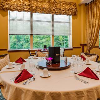 An elegantly set round dining table in a well-decorated restaurant with large windows.