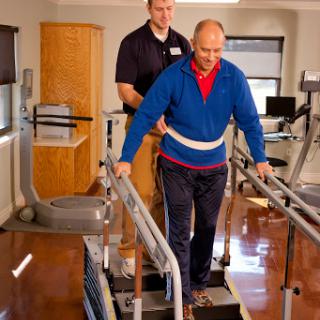 A healthcare professional assists an elderly patient during a physical therapy session, using a walking aid for support.