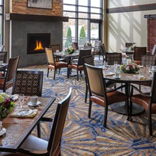 A cozy restaurant dining area with tables and chairs arranged near a fireplace.