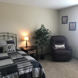A cozy bedroom with a bed, lamp, and recliner chair.