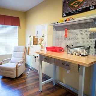 A bright and organized workshop area featuring a desk with tools, a comfortable chair, and natural light from a window.
