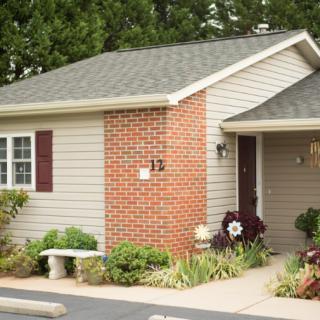 A small house with brick and siding exterior, surrounded by well-maintained landscaping and a bench in the front yard.