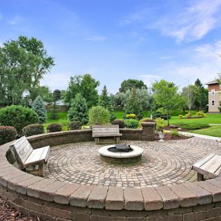 A serene outdoor space featuring a circular stone fire pit surrounded by benches, perfect for gatherings and enjoying nature.