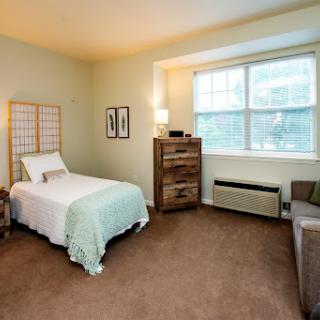 A cozy bedroom featuring a single bed, dresser, and large window, creating a bright and inviting atmosphere.