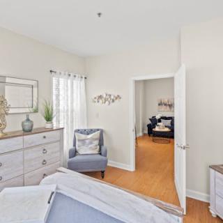 A cozy bedroom with a dresser, accent chair, and natural light streaming through the window.