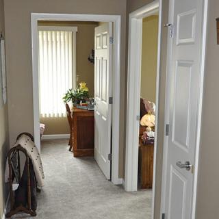 A hallway with multiple open doors leading to a room with a desk and window blinds.