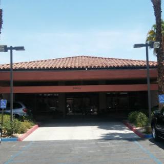 A sunny day at a modern building with a tiled roof and palm trees lining the parking area.