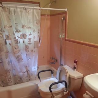 An accessible bathroom with a shower curtain, toilet, and bathtub equipped with grab bars.