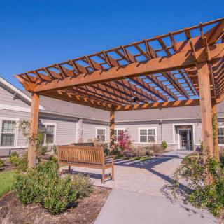 A wooden pergola with a bench in a landscaped garden outside a residential building.
