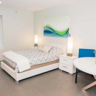 A modern, minimalist bedroom with a stylish bed, nightstand, and abstract artwork on the wall.