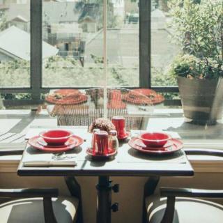 A sunlit dining table set with red dishes by a window, featuring a potted plant.