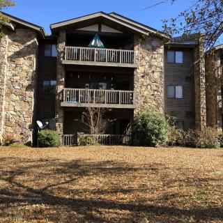 A multi-story apartment building with stone exteriors and balconies, set in a grassy area with surrounding trees.