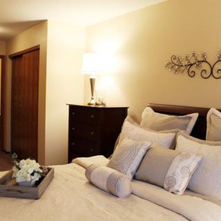 A cozy bedroom with a neatly made bed, decorative pillows, and elegant lighting.
