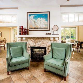 A cozy living room with two green armchairs in front of a stone fireplace, adorned with artwork and decor.