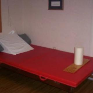 A therapy room featuring a red massage table with a pillow and paper towel.