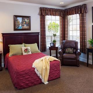 Cozy bedroom with a neatly arranged bed, armchair, and large windows.