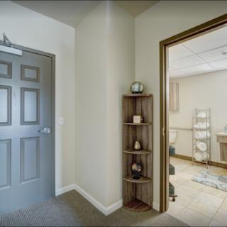 A view of a well-lit interior space featuring a hallway leading to a bathroom, complemented by decorative shelving.