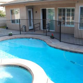 A backyard swimming pool with a safety fence and adjacent house.