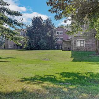 A residential building with a spacious lawn and surrounding trees under a clear blue sky.