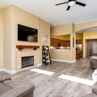 A cozy living room with a fireplace, television, and hardwood floors, featuring an open plan design with a view into the kitchen.