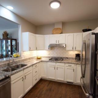 A modern kitchen featuring white cabinets and granite countertops, complemented by stainless steel appliances and a hardwood floor.