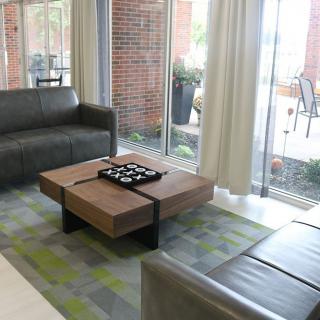 A modern living room with leather sofas and a wooden coffee table, set near large windows with curtains.