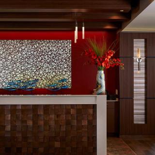 A modern reception area featuring a colorful artwork, a vase with red flowers, and sleek wooden textures.