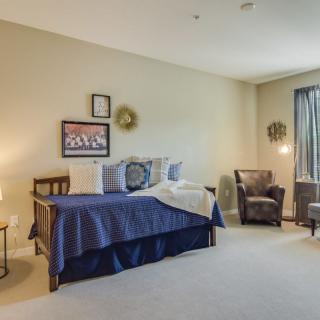 A cozy bedroom with a neatly made bed, armchairs, and soft lighting.
