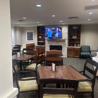 A cozy lounge area with a fireplace, television, and several tables and chairs.