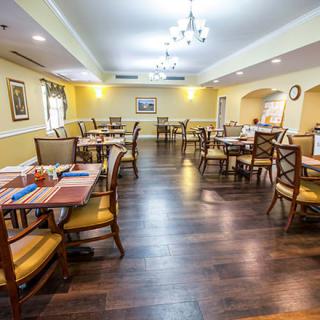 An inviting dining room with wooden chairs and tables, featuring elegant lighting.