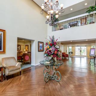 A spacious and elegantly decorated lobby featuring a chandelier, floral centerpiece, and artwork.