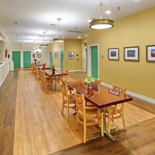 A bright dining area with wooden tables and chairs, featuring wood flooring and wall decorations.