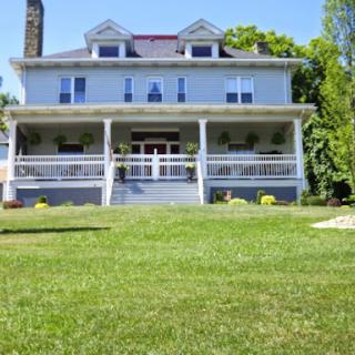 A charming blue house with a welcoming front porch and lush green lawn.