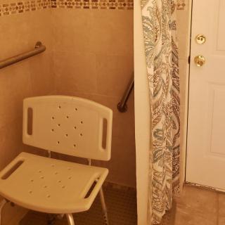 An accessible bathroom with a shower chair and grab bars.