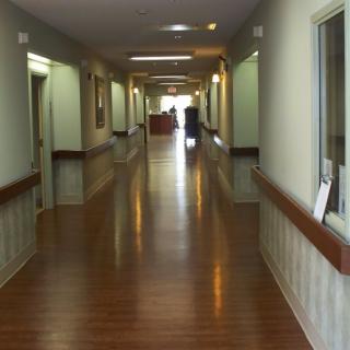A long, empty hallway in a healthcare facility with wooden floors and bright lighting.