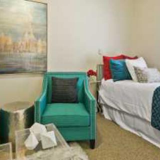 A cozy bedroom with a teal chair and decorative pillows, complemented by wall artwork.