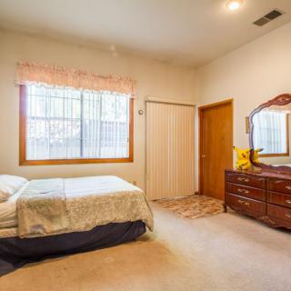A cozy bedroom with a bed, wooden dresser, and a curtained window.