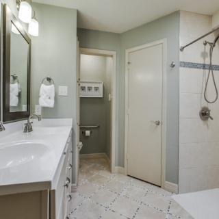 A modern bathroom with a sleek design featuring a large mirror, double sinks, and a walk-in shower.