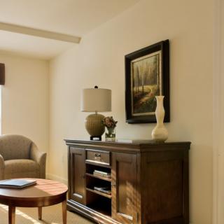 A cozy living room with a wooden cabinet, decorated with a lamp and vase, featuring a painting on the wall.