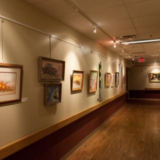 A hallway in an art gallery displaying various paintings on the wall.