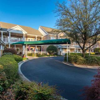 A picturesque retirement home with a circular driveway surrounded by well-maintained gardens and large trees.