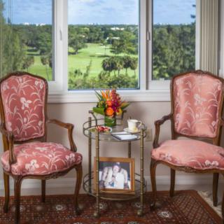 Two elegant chairs with a floral arrangement and tea set by a window overlooking a green landscape.