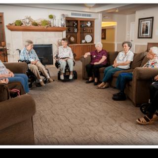 A group of seniors sitting in a comfortable living room setting, engaged in conversation.