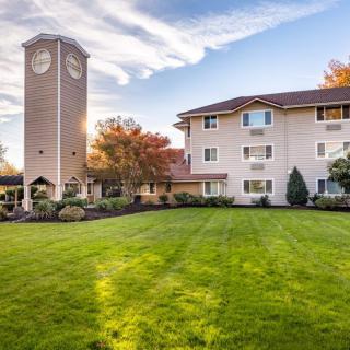 A scenic view of a building with a clock tower, surrounded by a well-maintained lawn and trees under a partly cloudy sky.
