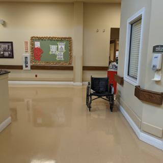 A quiet corridor in a healthcare facility featuring a wheelchair and bulletin board.