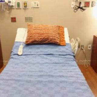 A hospital room featuring a neatly made bed with a blue blanket and orange pillow.