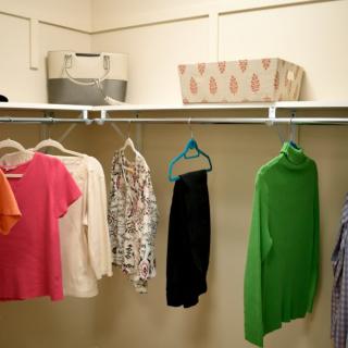 A neatly organized closet with colorful clothing on hangers and storage boxes on the shelf.
